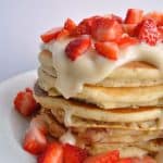 Stack of pancakes topped with cream cheese glaze and cut strawberries.