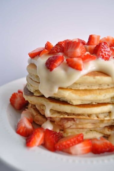 Stack of pancakes topped with cream cheese glaze and cut strawberries.