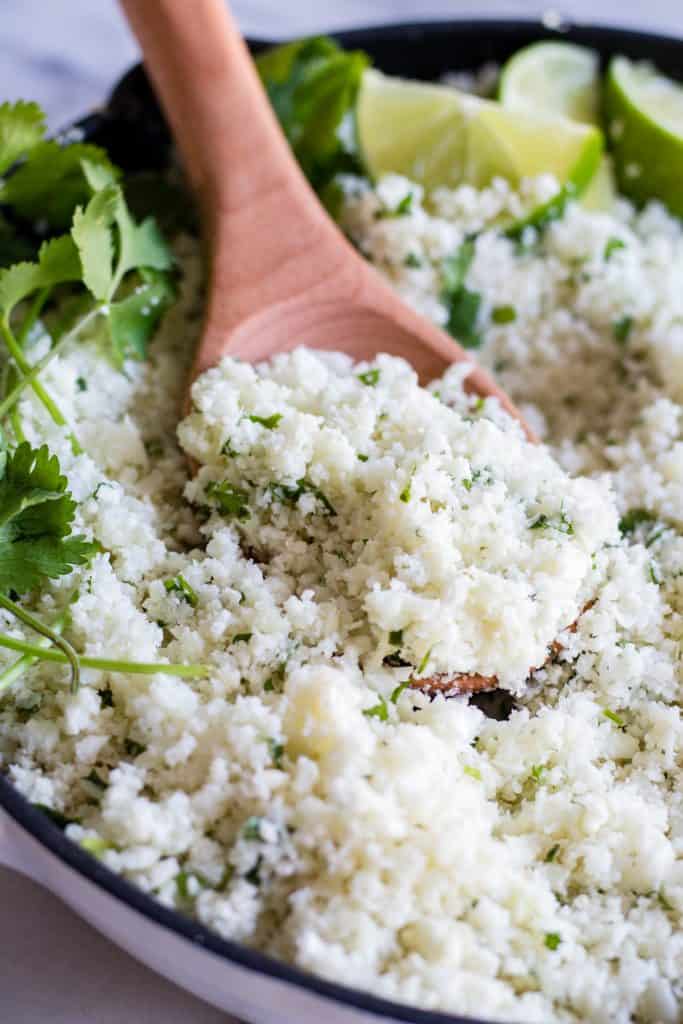 A wooden spoon scooping into a skillet with cilantro lime rice.