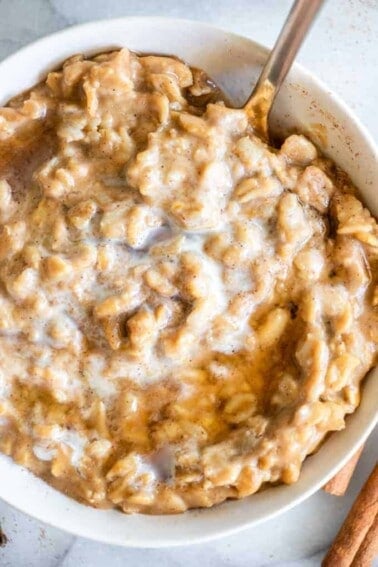 Pumpkin oatmeal in a bowl with heavy cream and maple syrup on top.
