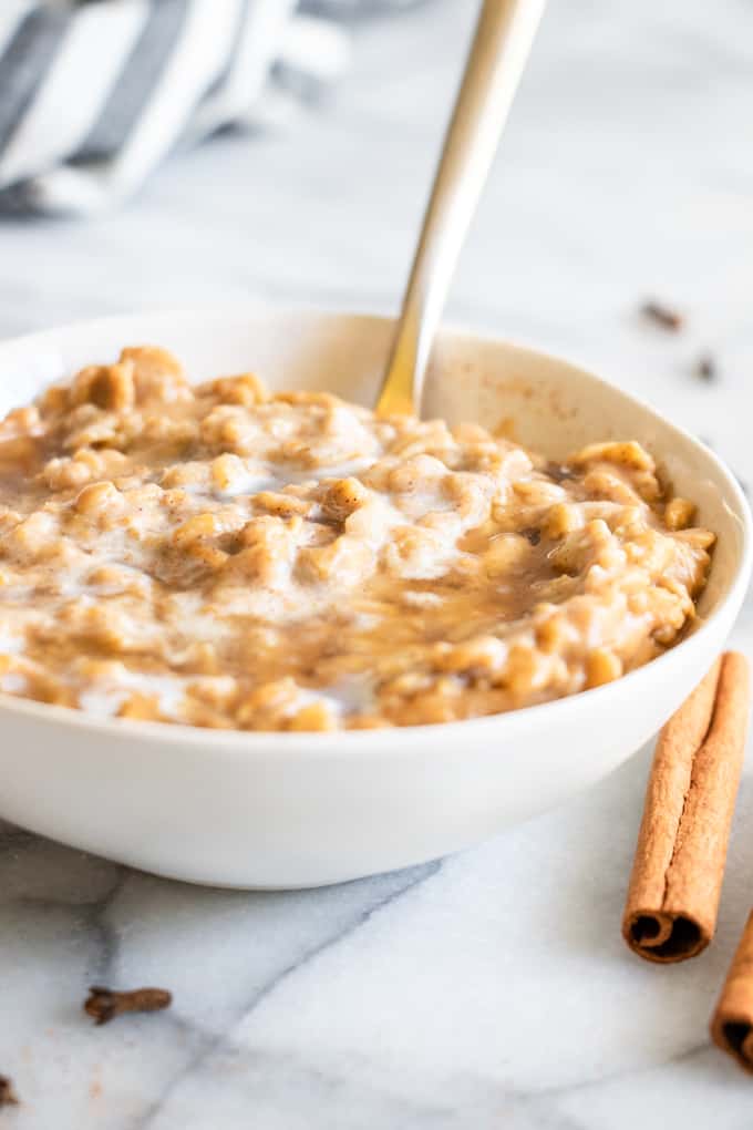 A bowl filled with pumpkin oatmeal, swirled with heavy cream, maple syrup and served up with a spoon.