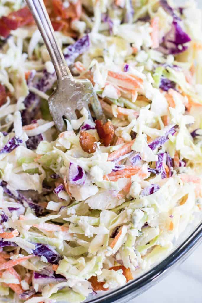  Large glass bowl filled with creamy blue cheese coleslaw topped with bacon. 