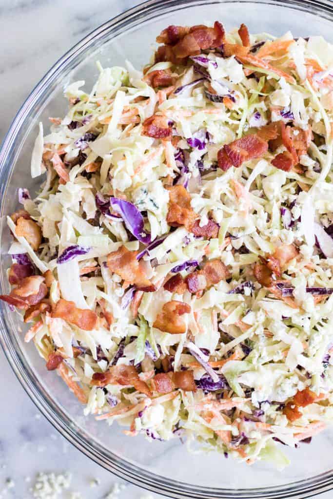Large glass bowl filled with creamy blue cheese coleslaw topped with bacon. 