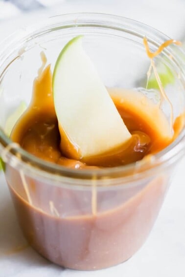 A jar filled with homemade caramel and an apple dipped in.