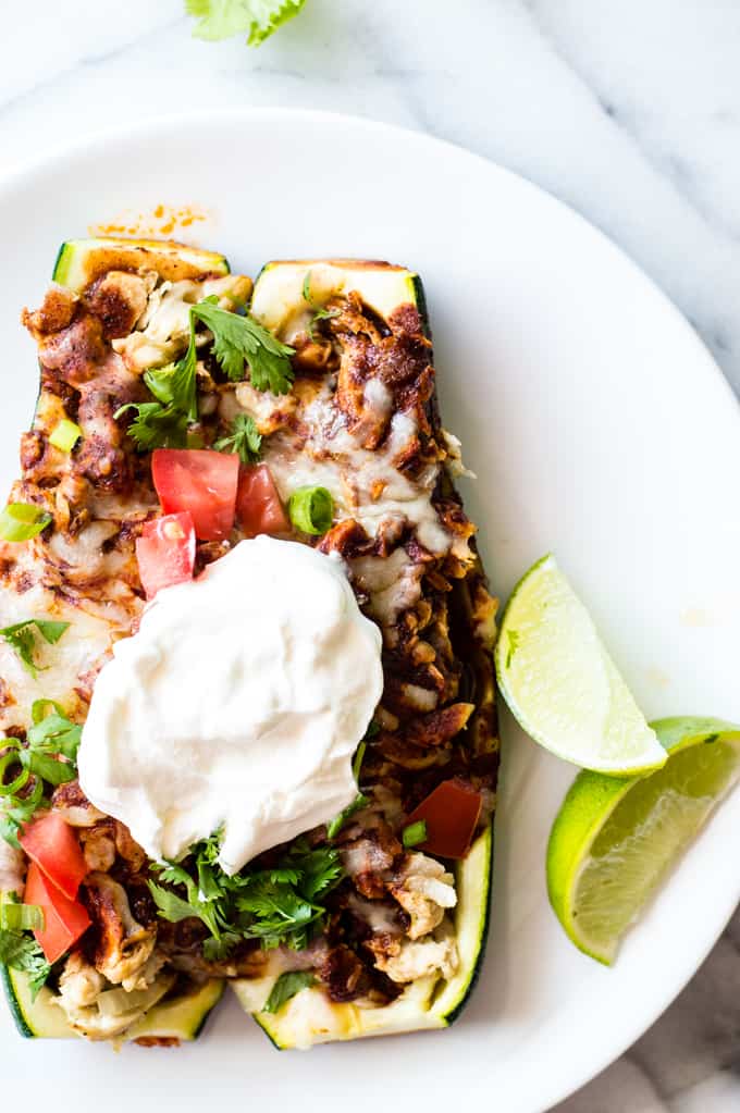 Two chicken enchilada zucchini boats on a plate topped with sour cream.