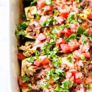 Baking dish filled with zucchini boats loaded with chicken enchilada filling. Topped with tomato and cilantro.