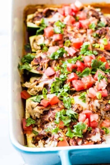 Baking dish filled with zucchini boats loaded with chicken enchilada filling. Topped with tomato and cilantro.