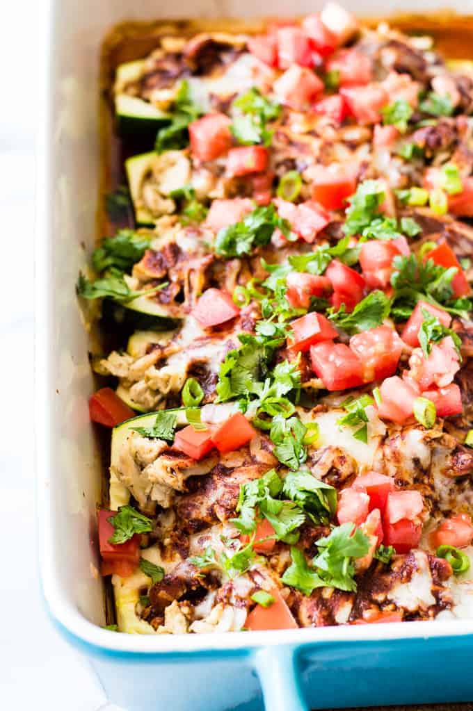 Baking dish filled with zucchini boats loaded with chicken enchilada filling. Topped with tomato and cilantro. 
