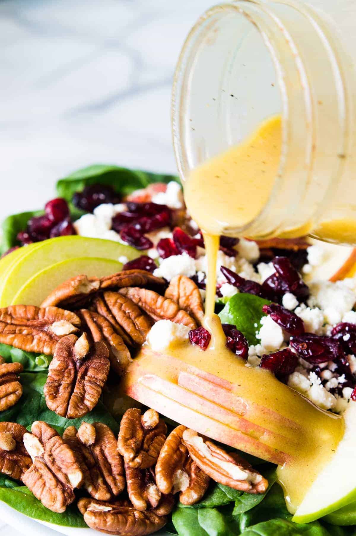 Autumn Apple Salad in a large salad bowl being drizzled with Maple Dijon Vinaigrette.