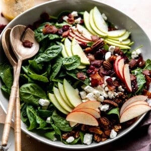 Large white bowl of apple salad served with wooden serving spoons.