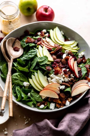 Large white bowl of apple salad served with wooden serving spoons.