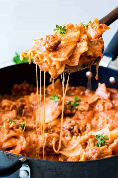 Wooden spoon scooping up lasagna pasta with strings of cheese coming back down to the skillet.