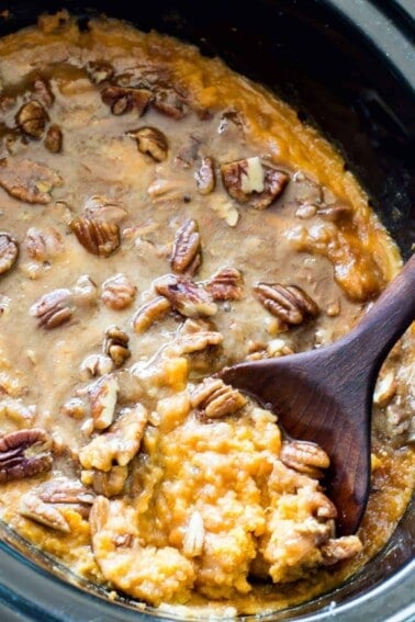 A slow cooker filled with sweet potato casserole topped with brown sugar pecan topping.