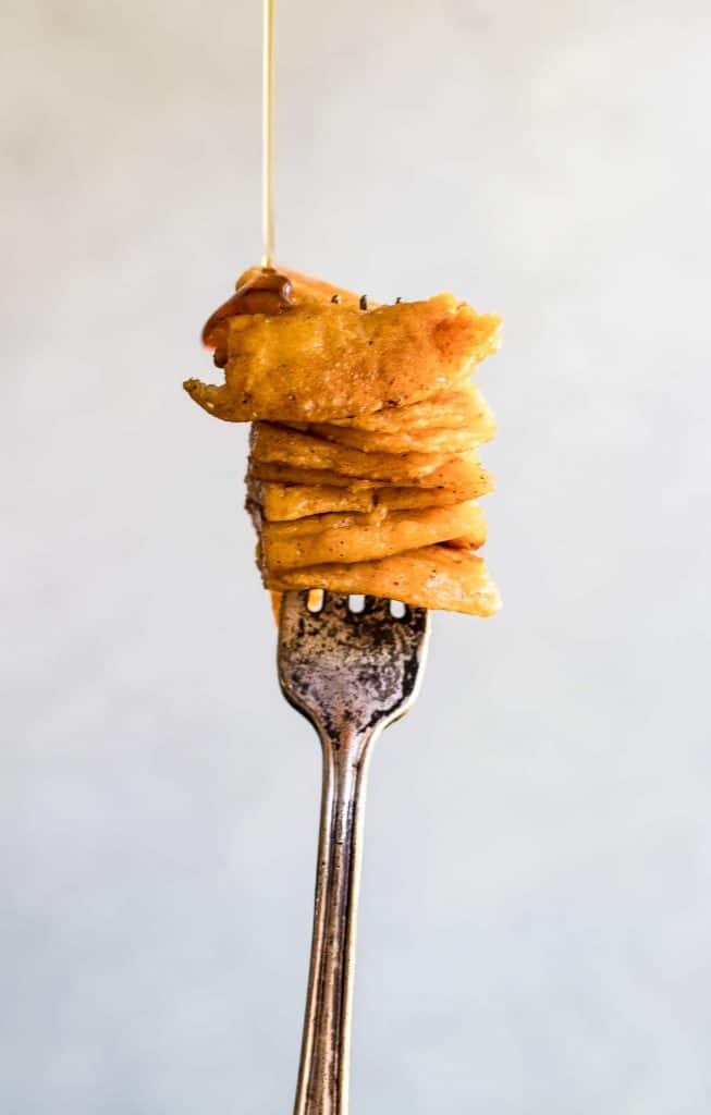 Fork being held up with a bite of stacked sweet potato pancakes and syrup being drizzled over it. 