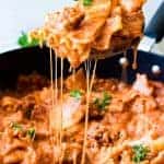 Wooden spoon scooping up lasagna pasta with strings of cheese coming down.
