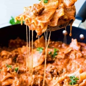 Wooden spoon scooping up lasagna pasta with strings of cheese coming down.