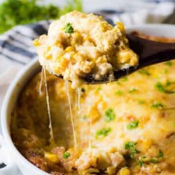 A spoon scooping out corn casserole, showing the cheese strings pulling away!
