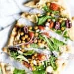 Close up of sliced flatbread pizza layered with hummus and toppings.