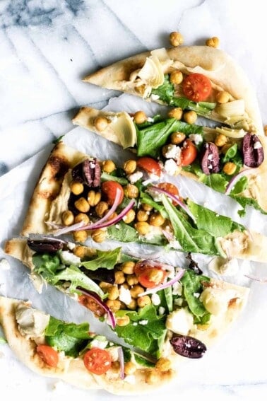 Close up of sliced flatbread pizza layered with hummus and toppings.