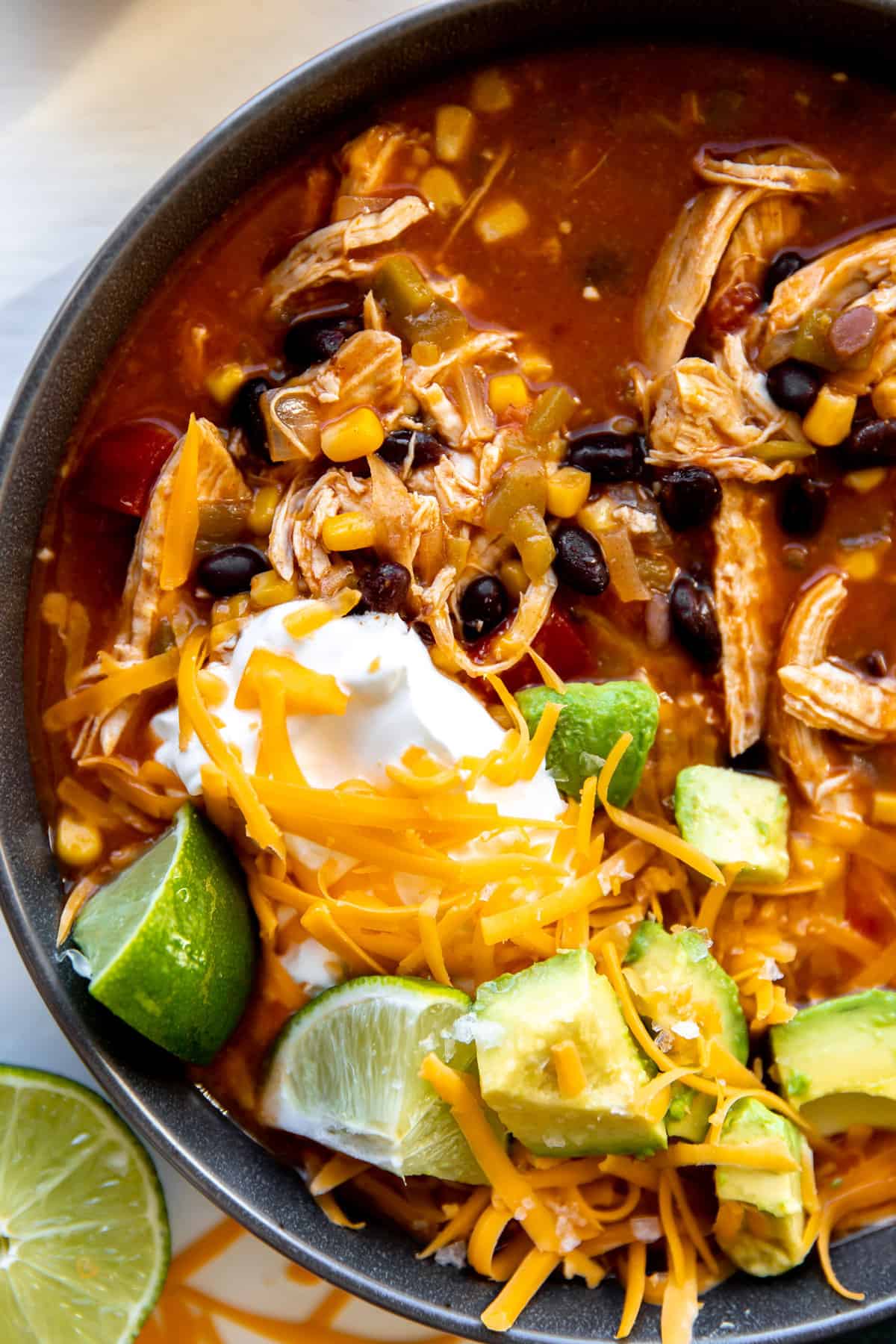 Up close view of chicken enchilada soup with sour cream and avocado on top.