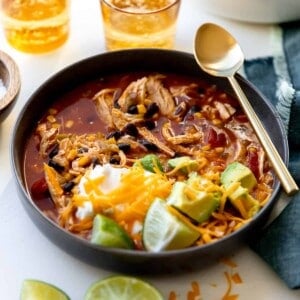 Bowl of chicken enchilada soup served with a spoon and glasses nearby.