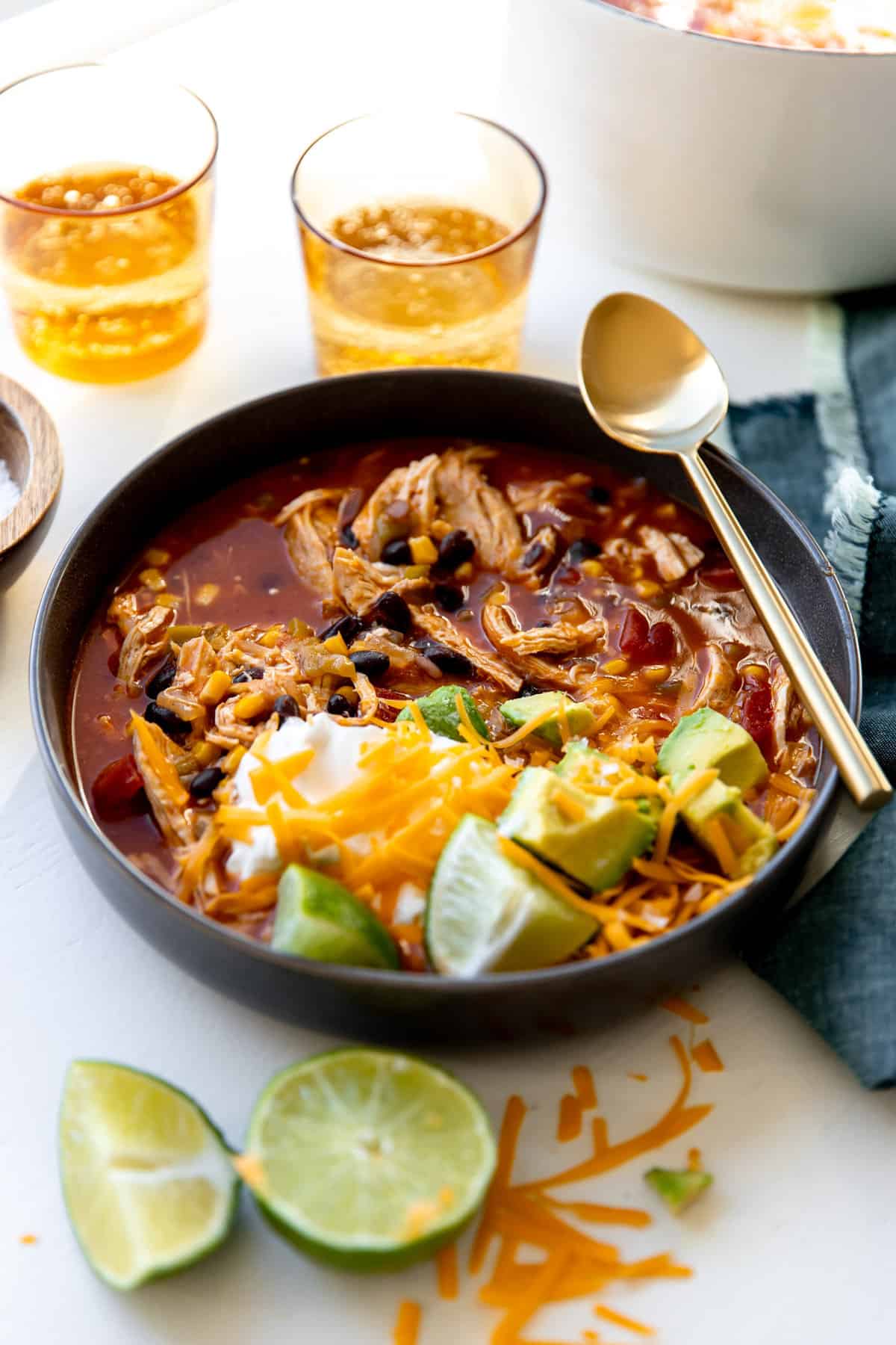 Bowl of chicken enchilada soup served with a spoon and glasses nearby.