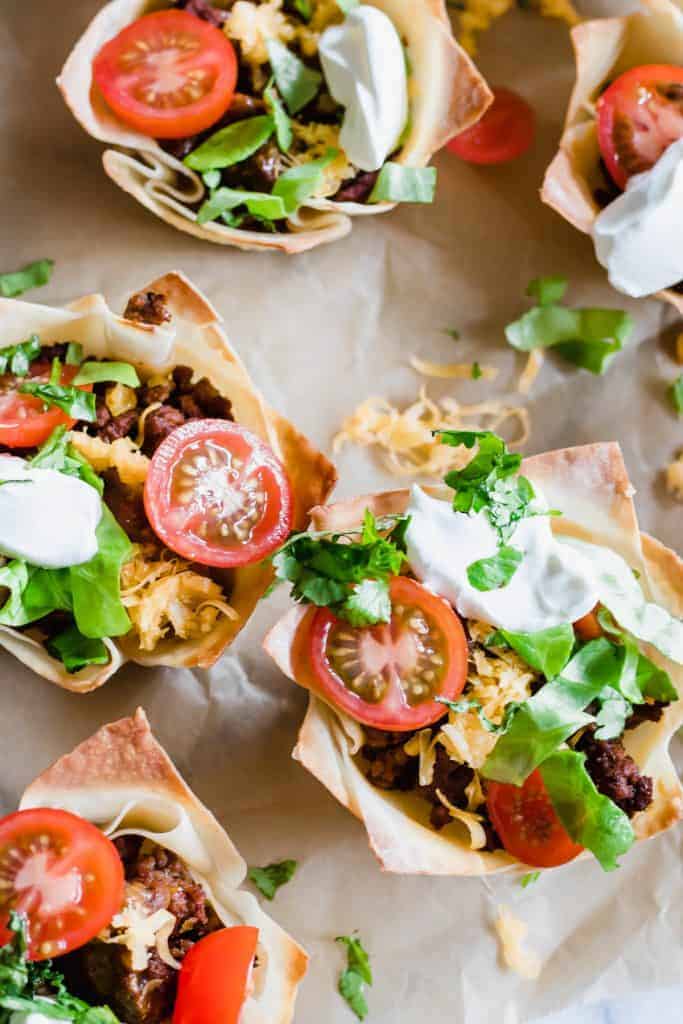 Overhead view showing crunchy wonton cups filed with uicy taco meat, melty cheese, shredded lettuce, tomato and sprinkled cilantro. 