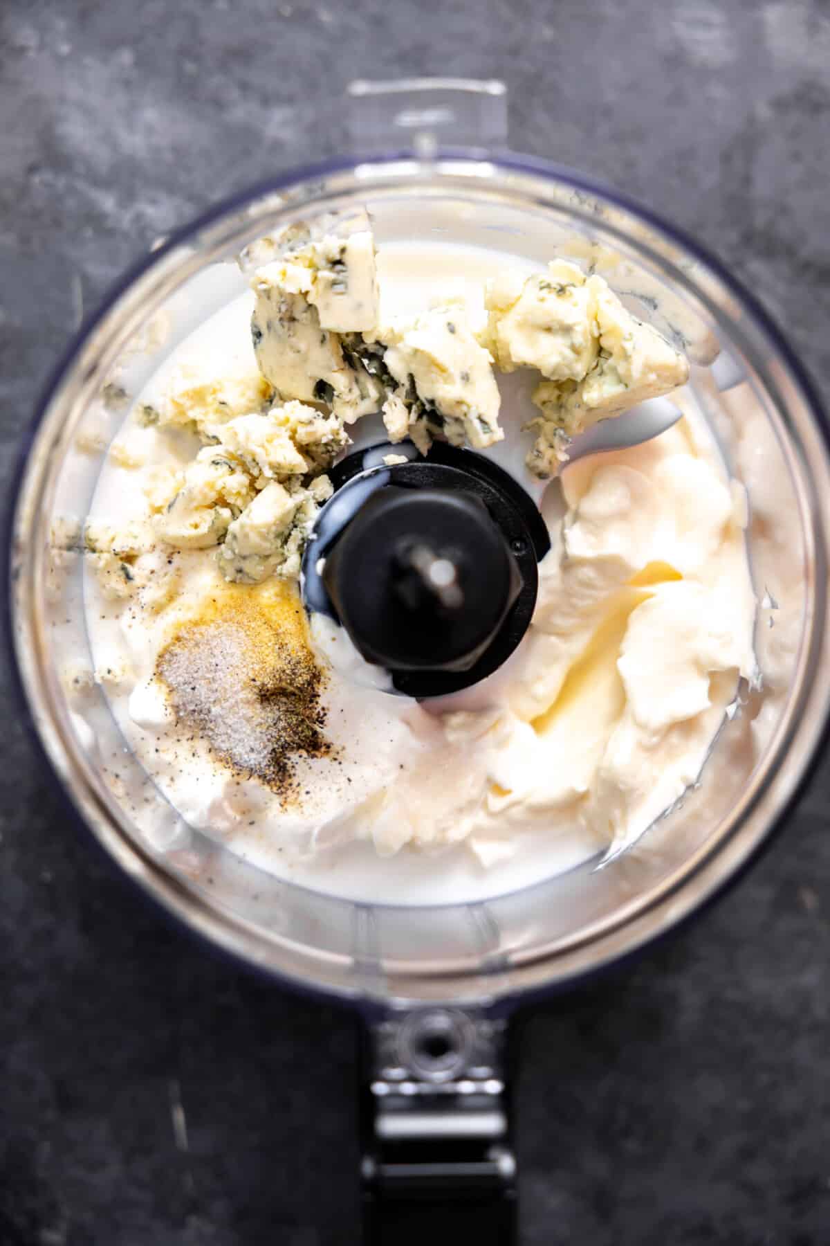 Food processor with ingredients to make homemade blue cheese dressing before blending.