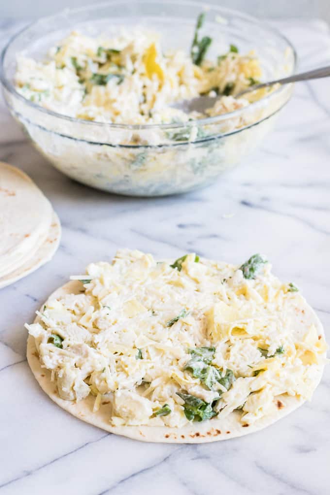 One flour tortilla loaded up with spinach and artichoke chicken mixture to be made into a quesadilla. 