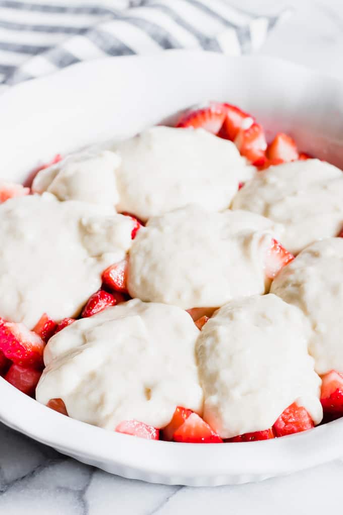 Pie dish filled with fresh strawberries and cobbler batter spooned on top before baking.