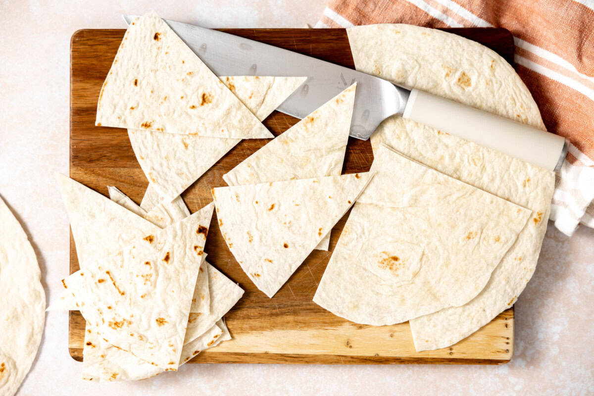 Flour tortillas being cut into triangular chips. 