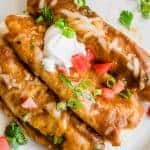 Overhead view of three chorizo enchiladas on a plate topped with sour cream, cilantro and tomato.