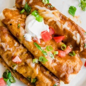 Overhead view of three chorizo enchiladas on a plate topped with sour cream, cilantro and tomato.