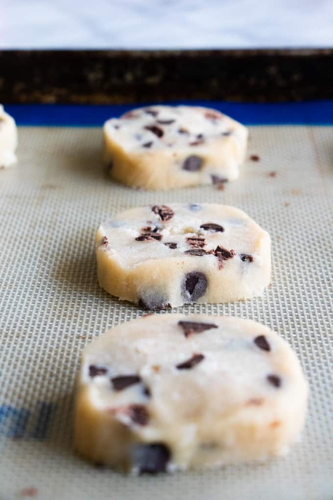 Slices of chocolate chip shortbread cookies on a baking sheet lined with a silicone baking mat.