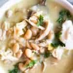 Close up image of green Chile enchilada soup, topped with sour cream and fresh cilantro.