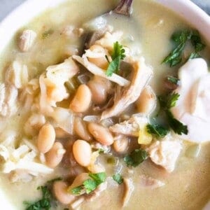 Close up image of green Chile enchilada soup, topped with sour cream and fresh cilantro.
