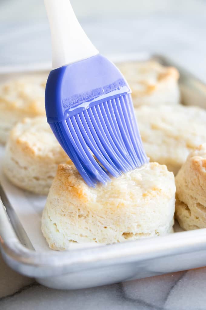 Baked homemade biscuits being brushed with melted butter.