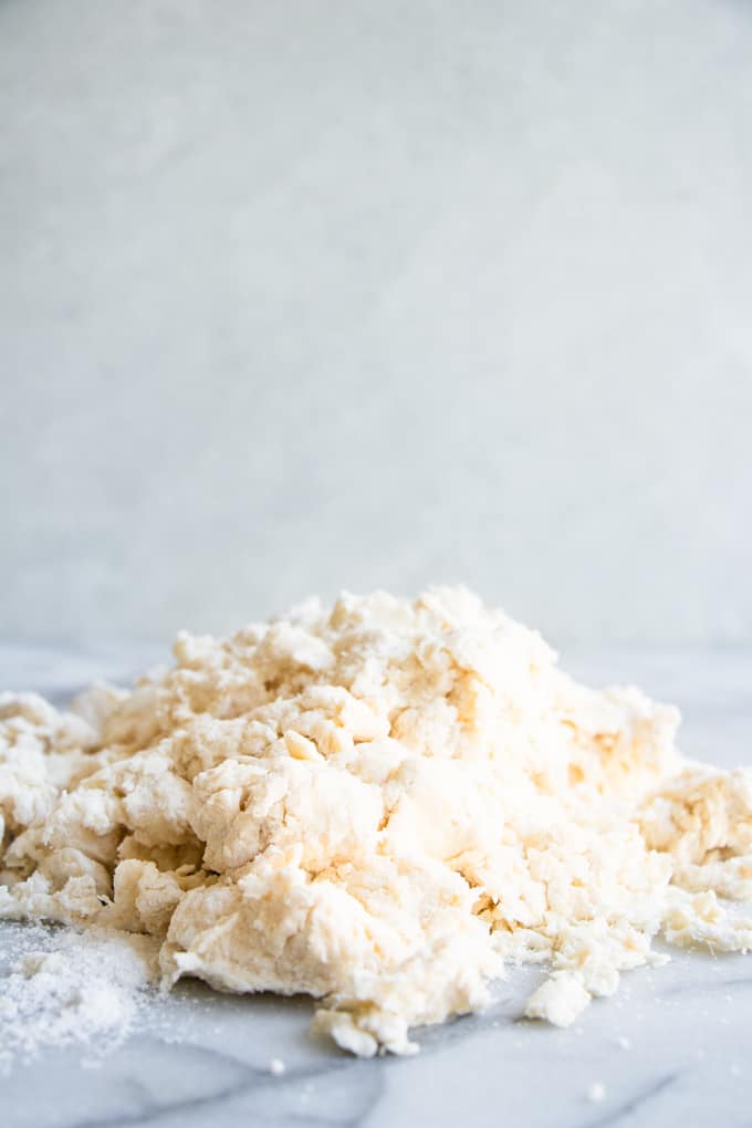 Crumbly biscuit dough on a marble slab ready to be gently pressed together for homemade biscuits.