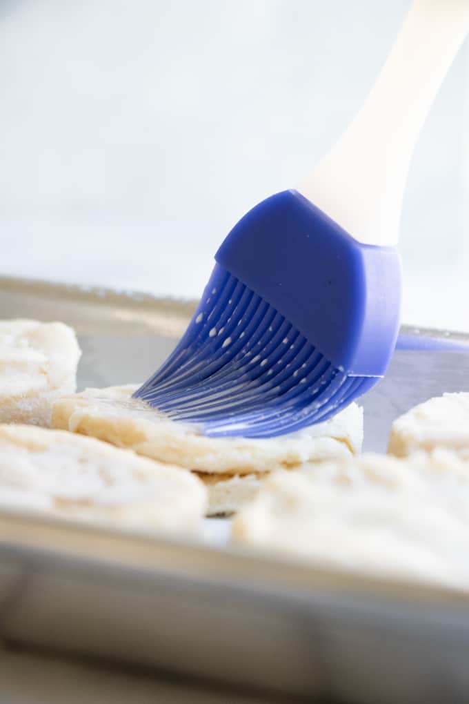 Homemade biscuit dough being brushed with cream prior to baking.
