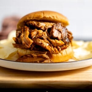 Slow cooker pulled pork on a hamburger bun served with potato chips.