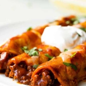Homemade Beef Enchiladas served on a plate with diced cilantro and a swirl of sour cream on top.