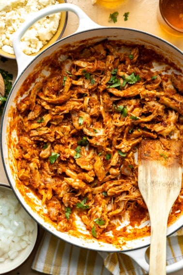 Chicken Tinga served in a skillet, with tortillas, onions and other toppings on the side