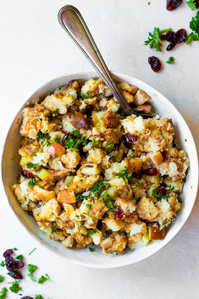 Cranberry Apple Stuffing served in a white bowl and a large spoon. Garnished with fresh parsley.