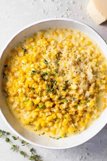 Bowl of creamed corn topped with shredded parmesan cheese and fresh thyme.
