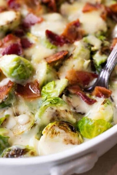 Baked Creamy Brussels sprouts in a baking dish with a spoon scooping up.