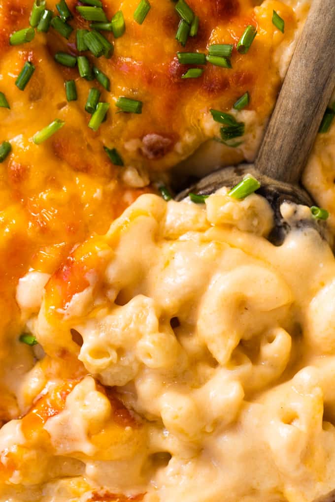 Wooden spoon in homemade baked macaroni and cheese showing still creamy consistency after baking.