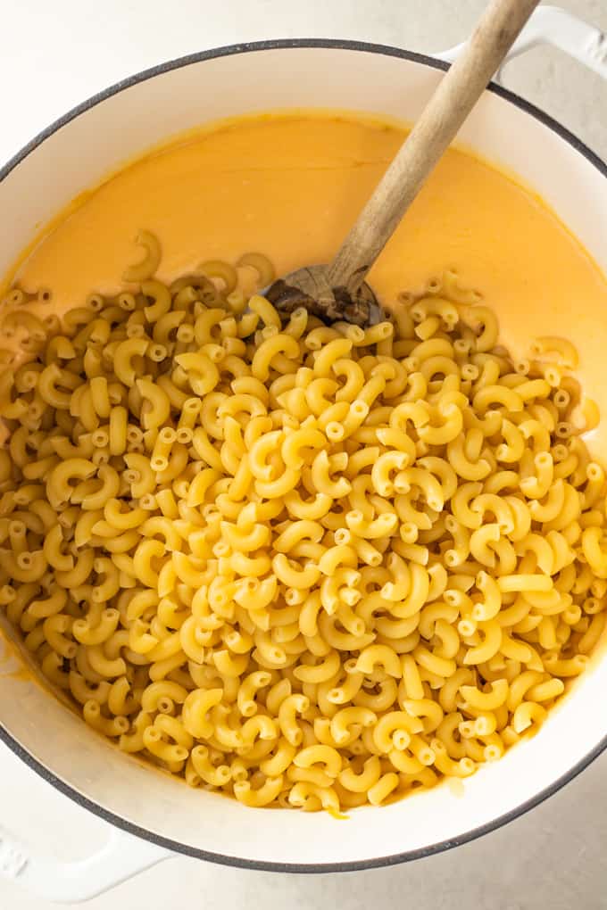 Elbow macaroni noodles added to a large dutch oven of homemade cheese sauce for macaroni and cheese.