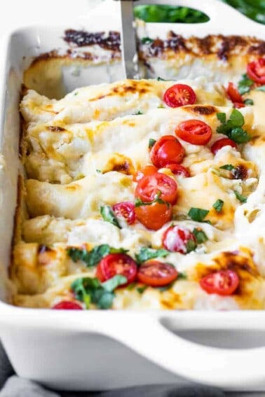 Baking dish filled with cheese breakfast enchiladas topped with diced tomatoes and cilantro.
