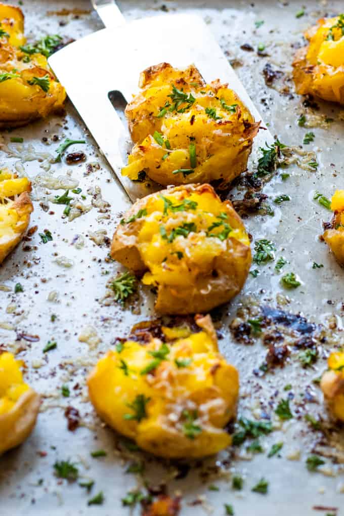 Smashed potatoes on a baking sheet being picked up with a spatula.