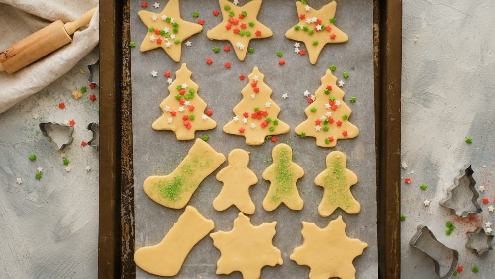 Sugar cookies being decorated with sprinkles ready to bake.